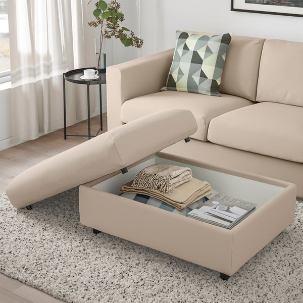 Modern living room with beige VIMLE sectional sofa, geometric throw pillow, and storage footstool displaying blankets and magazines.