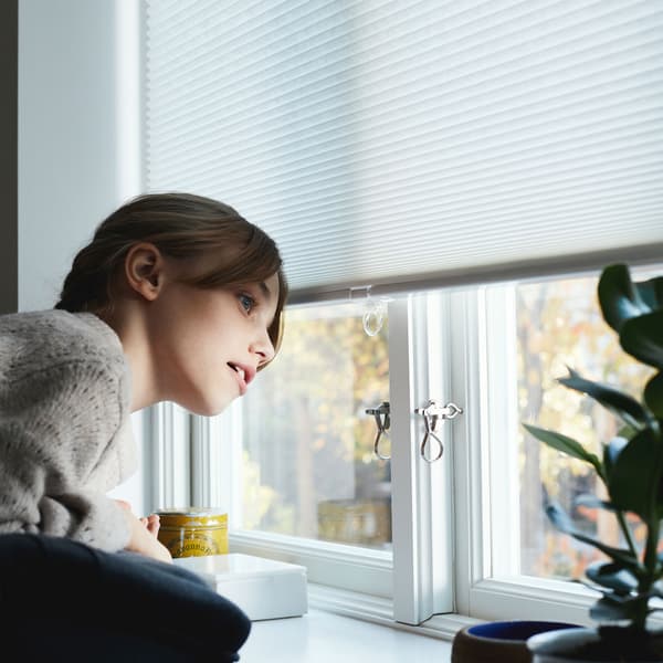 블라인드 한 부분을 내려 창문 밖을 내다보고 있는 스웨터를 입은 한 여자아이