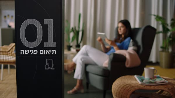 תיאום פגישה - אישה יושבת על כורסה בסלון ומחזיקה טאבלט ביד