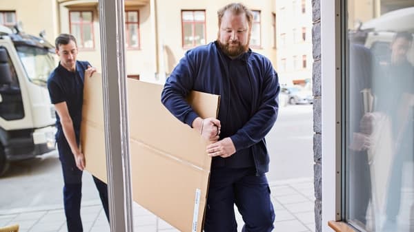 2 men carry a large parcel through the door.