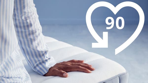 90 Nächte Testschlafen Symbol, im Bild eine Person, die auf einer Matratze sitzt.