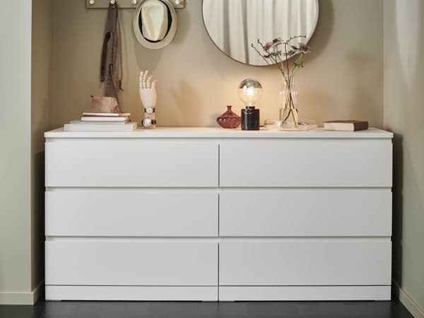 A 6-drawer white MALM dresser with various items sitting on top and a round mirror above it.