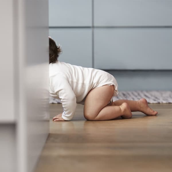 A baby wearing a white onesie crawling on the floor.
