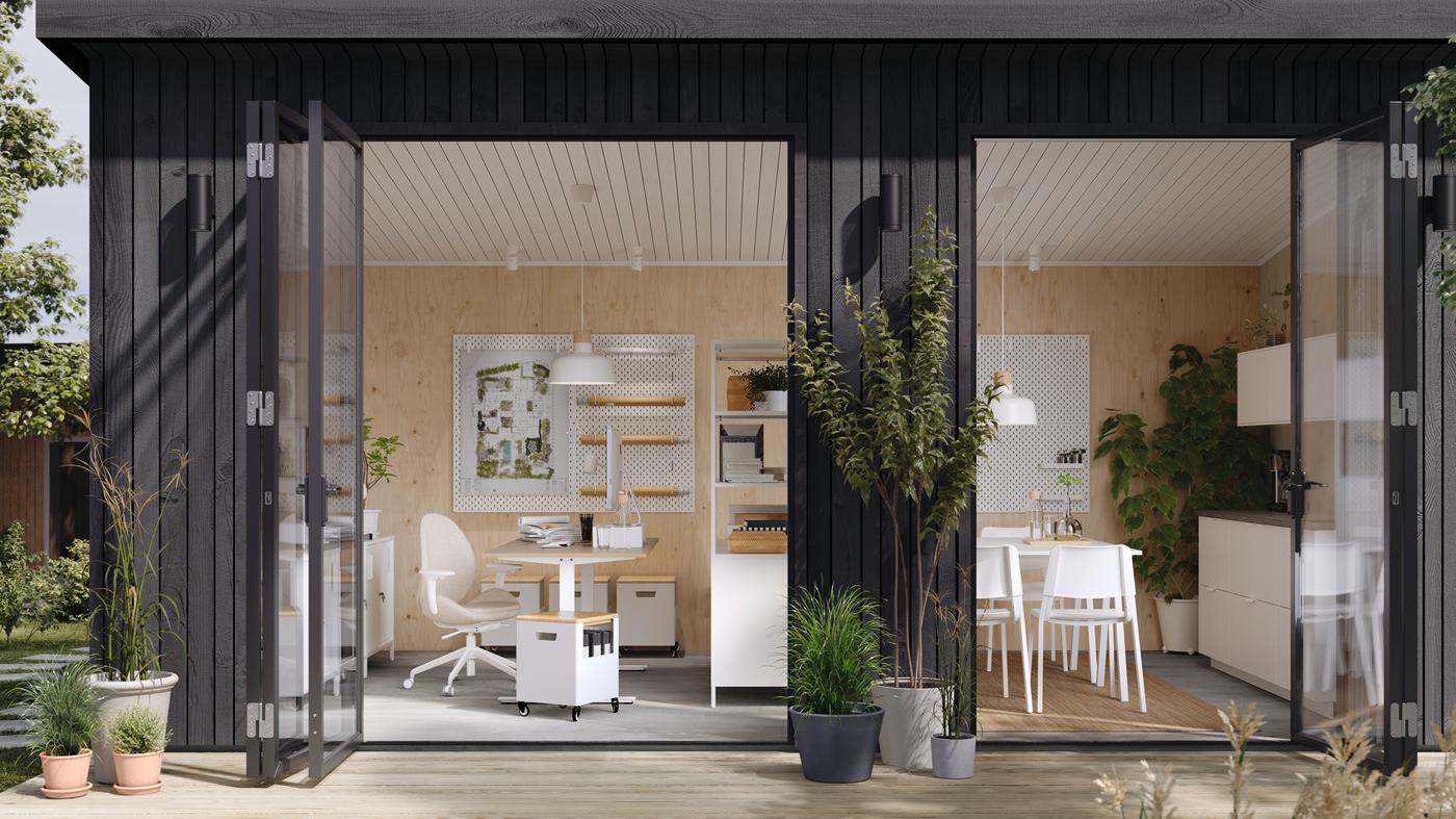 A backyard studio with open doors showing a desk and chair work area, open shelving divider and a communal kitchen area.