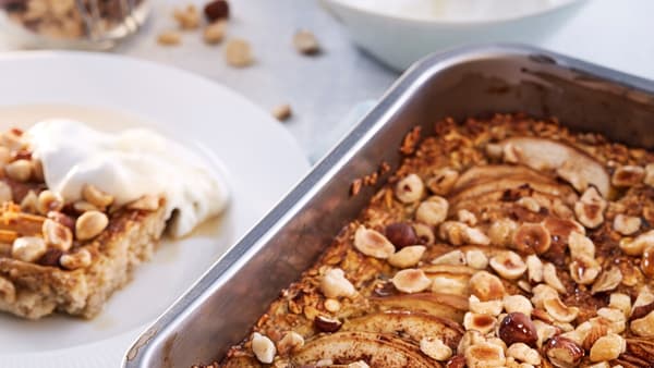 A baking tin containing cooked HJÄLTEROLL porridge by a white plate with a slice of porridge and a dollop of yoghurt on it.