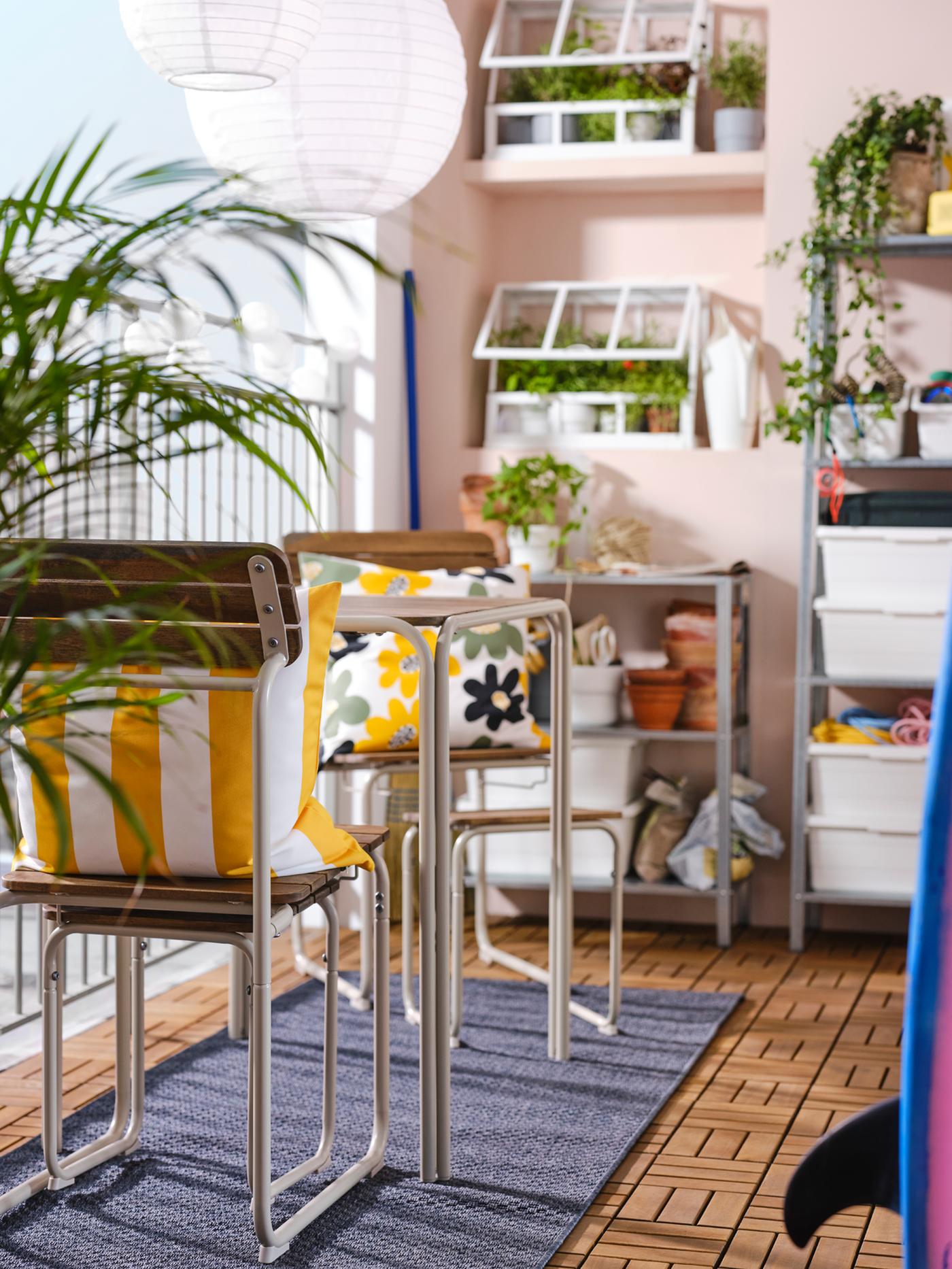 A balcony with pink walls featuring a FURUÖN dining table with 2 chairs and 2 footstools, shelving units and a greenhouse.