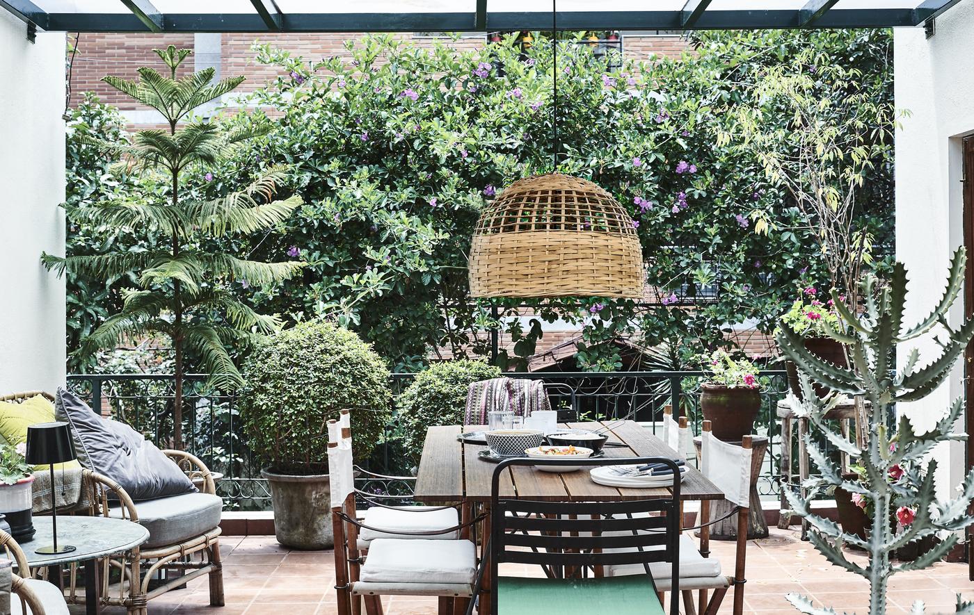 A balcony with plants, chairs, table and pendant lamp.