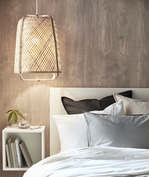A bamboo lamp hanging low over a bed and a square storage unit on the wooden wall behind.