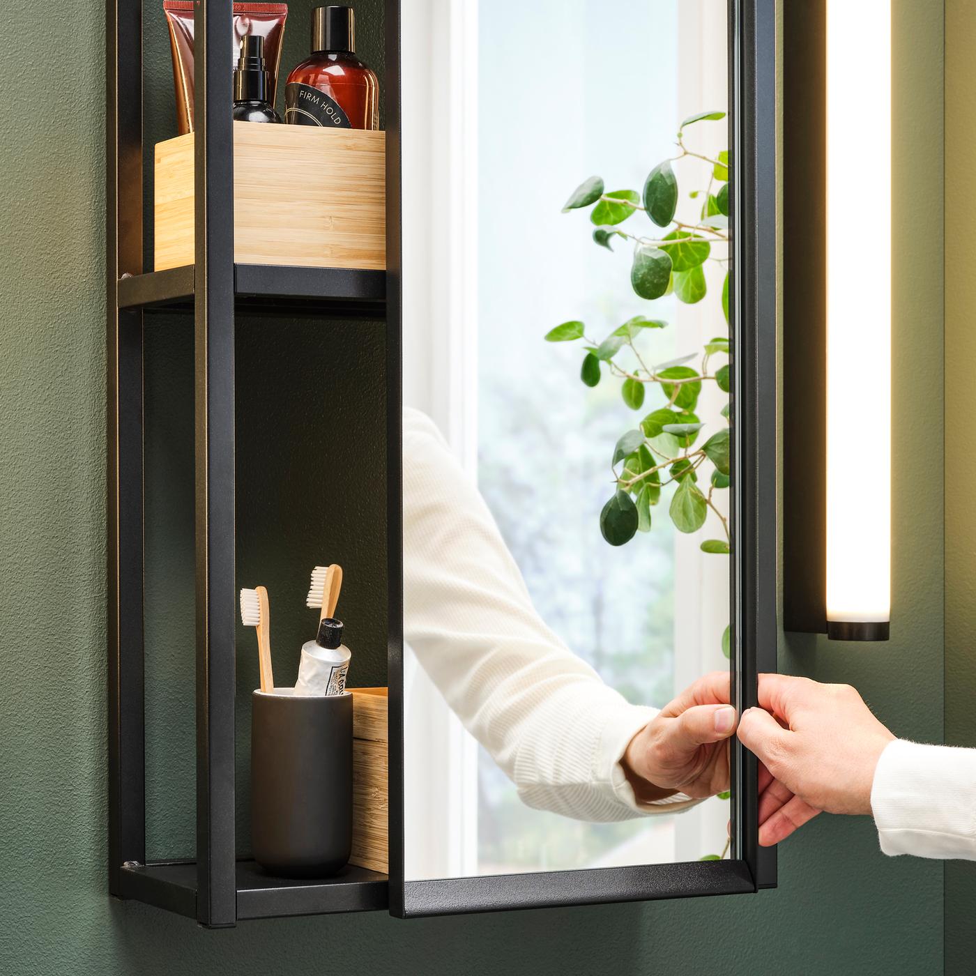 A bathroom with a wall-mounted ENHET mirror cabinet. Boxes with beauty products and a toothbrush holder sit on the shelves.