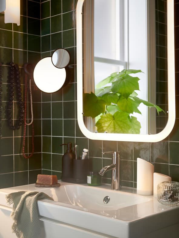 A bathroom with a white mirror with integrated lighting over a wash-stand, plus light green guest towels and a potted plant.