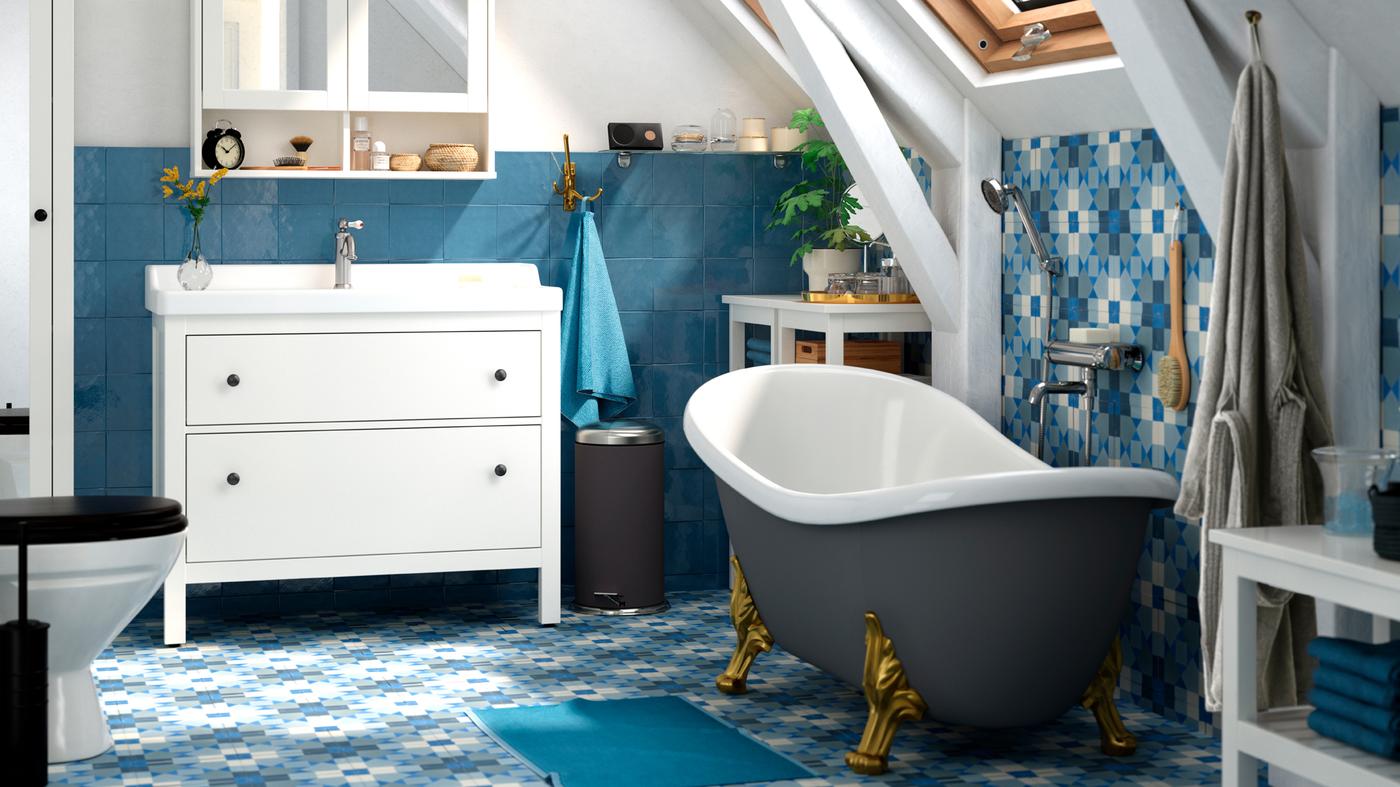 A bathroom with blue floor and wall tiles, a free-standing bath tub, and white wash-basin with mirrored cupboards above.