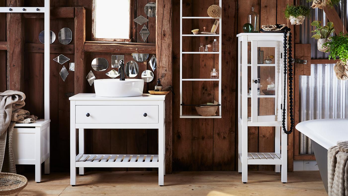 A bathroom with dark wooden walls, covered in small and oddly shaped mirrors and white HEMNES bathroom furniture.