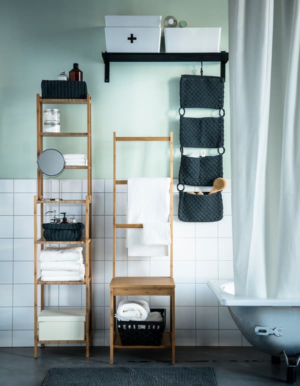 A bathroom with white tiles and light-green wall. Bamboo wood furniture stores towels and accessories.