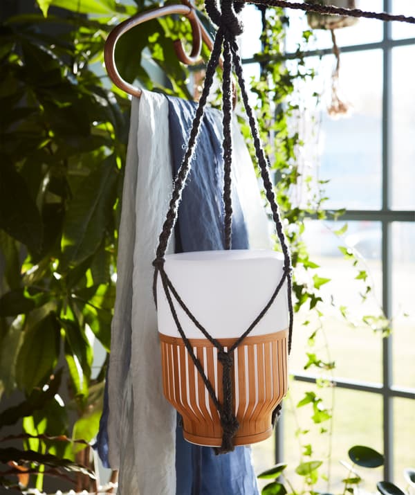 A battery charged MULLBACKA LED table lamp hanging freely, surrounded by plant greenery.