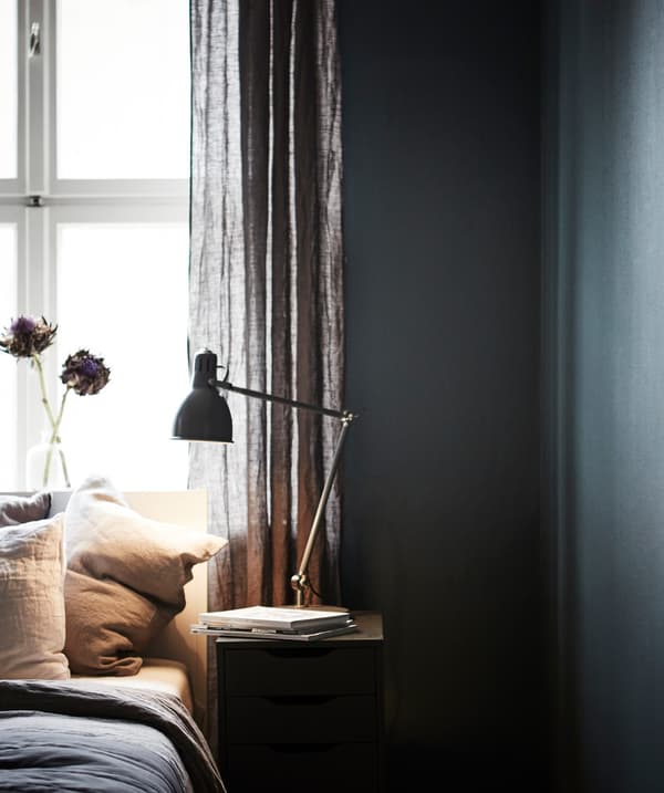  A bed and bedside table in front of a window in a bedroom painted dark blue/green.
