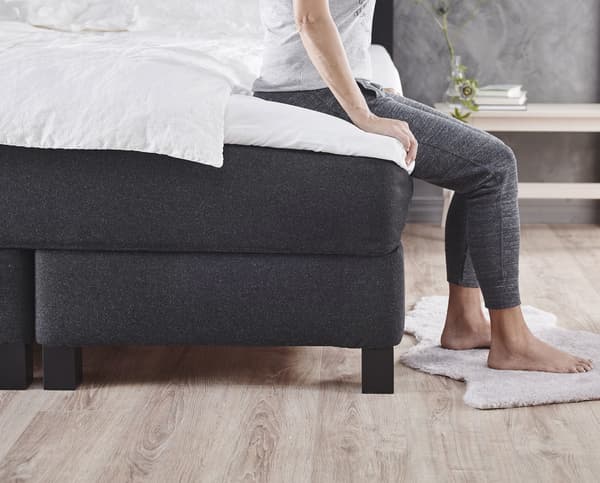 A bed base with mattress on top that a person is sitting on.
