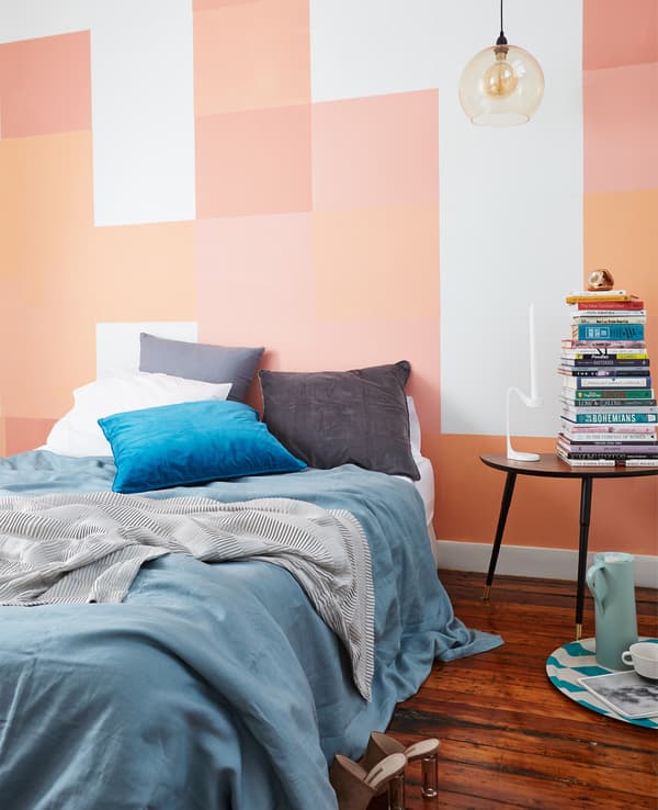 A bed dressed with blue and grey textiles against a wall painted with pink, coral and orange squares.