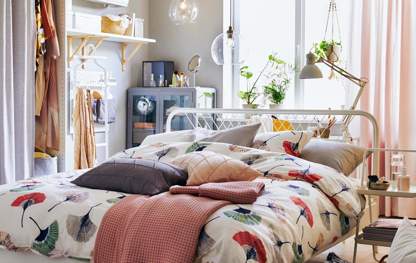 A bed dressed with floral bedding in the middle of a room with storage and shelves along the walls.