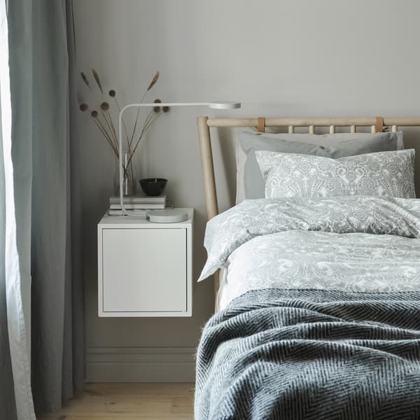 A bed dressed with layers of grey patterned bedding and a white bedside table.