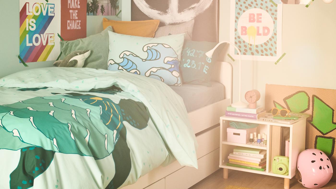 A bed is dressed in a turquoise blended cotton BLÅVINGAD turtle duvet cover set; posters cover the walls around the bed.