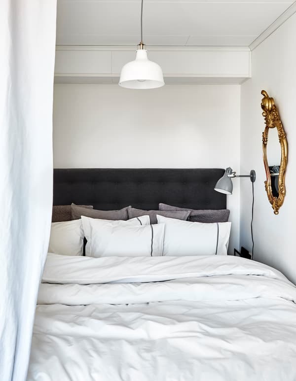A bed is made up with lots of fluffy pillows and thick comforters in neutral shades.