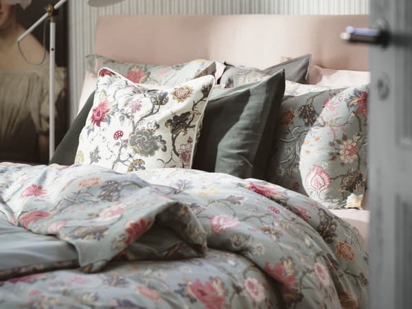 A bed made with a floral pink and light green duvet cover and pillows to match.
