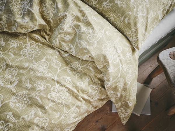 A bed made with IKEA JUNIMAGNOLIA bed linen in cotton with a classic, white and green flower print.