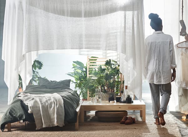 A bed under a white draped canopy with indoor plants.