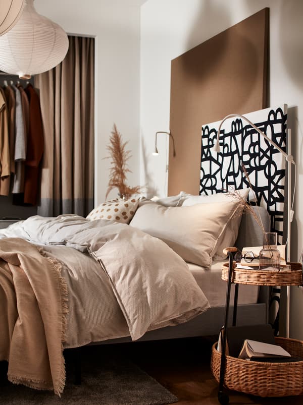 A bed with beige bed linen, and a wall panel made from particle board covered with black and white SKUGGBRÄCKA metre fabric.