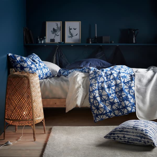 A bed with blue and white patterned bedding and a bamboo floor lamp in a room with dark blue walls.