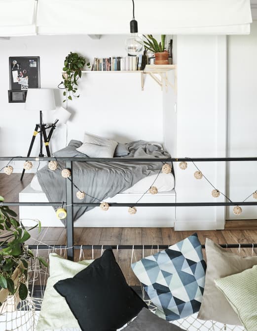 A bed with bookshelf above it and cushions on a large hammock.