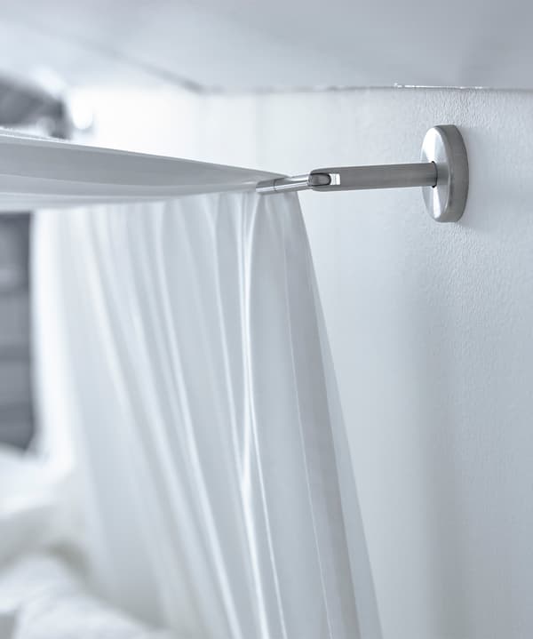 A bed with white linens sits under a sloped ceiling, and white textile hangs from the ceiling to create a canopy.