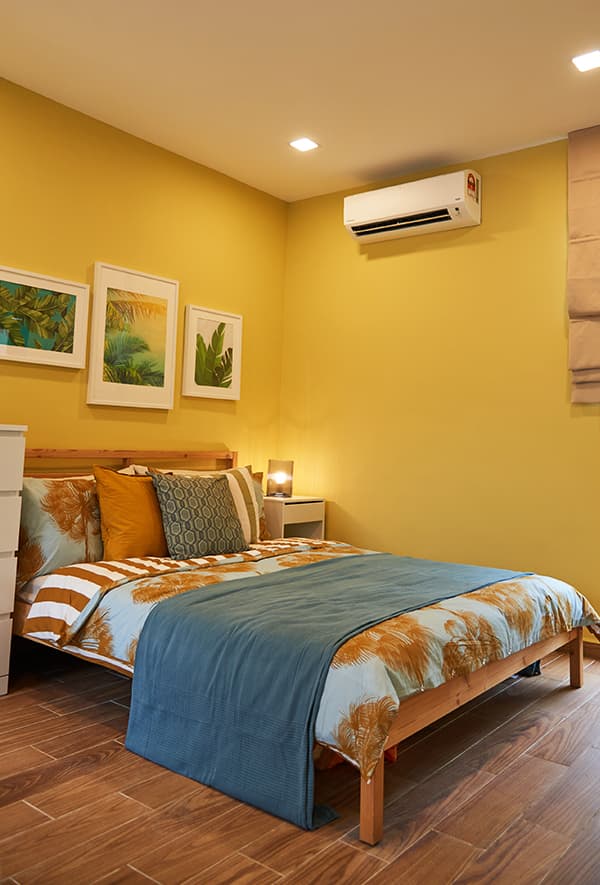 A bed with white picture frames hung on top in a yellow room. 