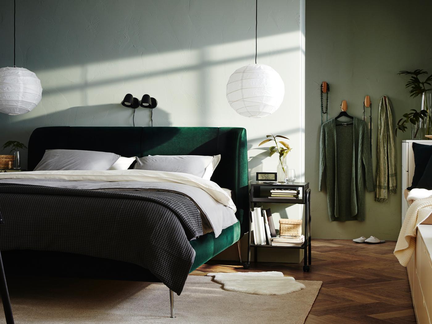 A bedroom where a green TUFJORD upholstered bed stands against a wall and two pendant lamps hang from the ceiling.
