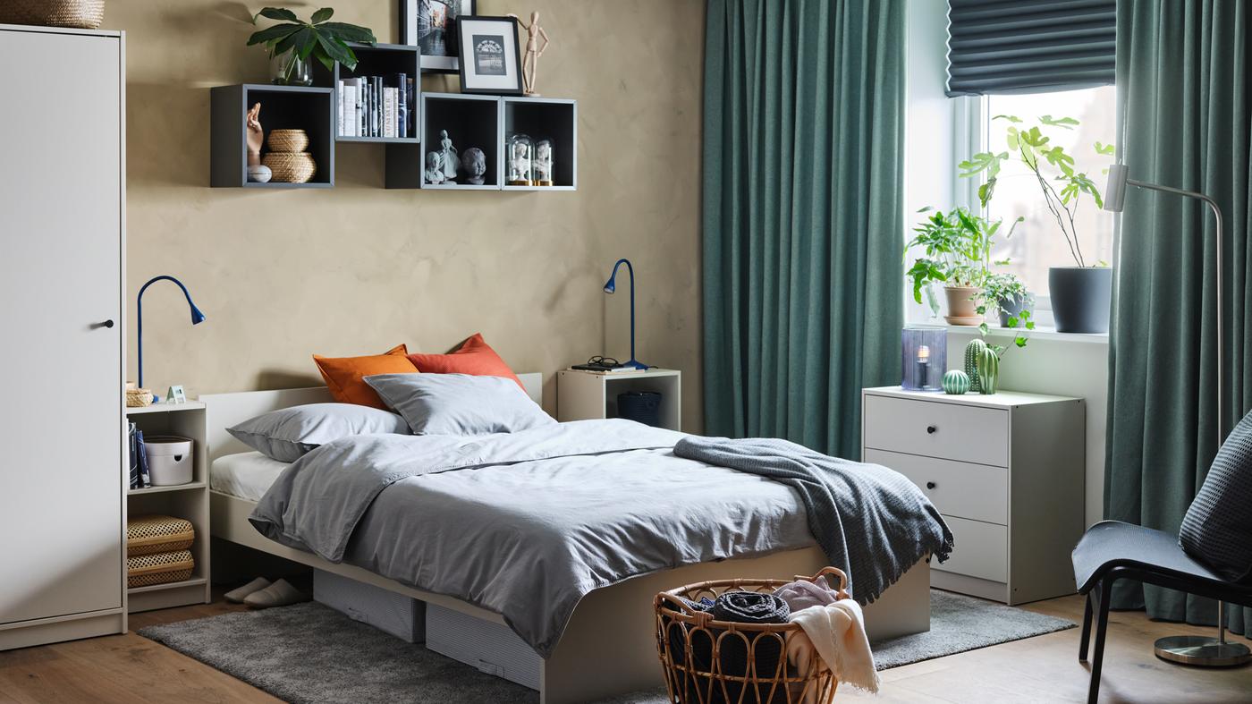 A bedroom with a bed frame with headboard, wardrobe, bedside table and chest of drawers all with a light beige colour.