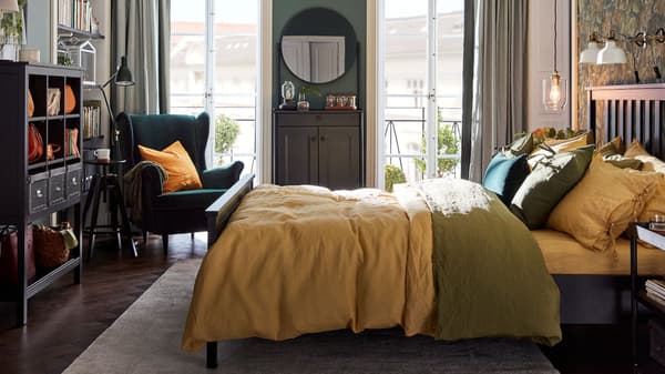 A bedroom with a bed with pillowcases and quilt covers in green and yellow, a cabinet with a mirror and a green wing chair.