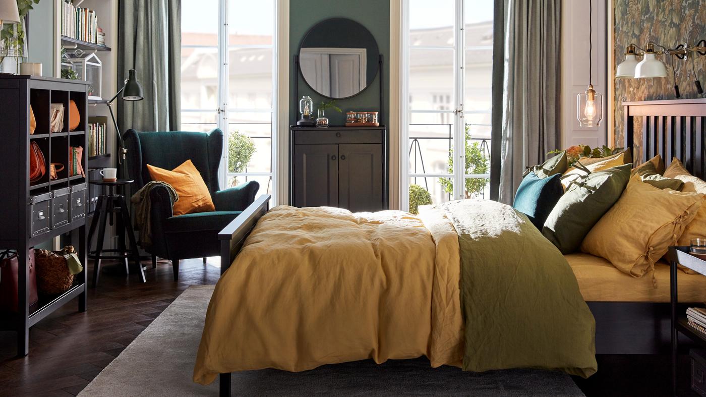 A bedroom with a HEMNES bed with colourful bed linen, a green STRANDMON chair in one corner and two balcony doors.