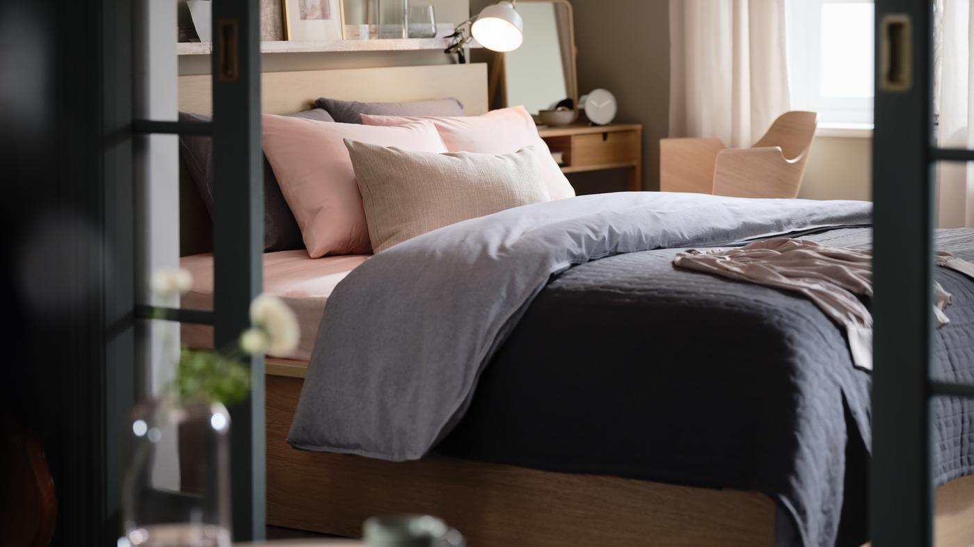 A bedroom with a MALM bed, dark-blue KOPPARBLAD bed linen, a NORDKISA dressing table, and a FJÄLLBERGET conference chair.
