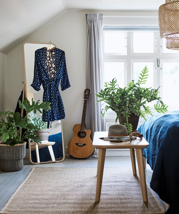 A bedroom with a woven ceiling lamp and rug, freestanding mirror with dress hanging on it and a bench at the end of the bed.