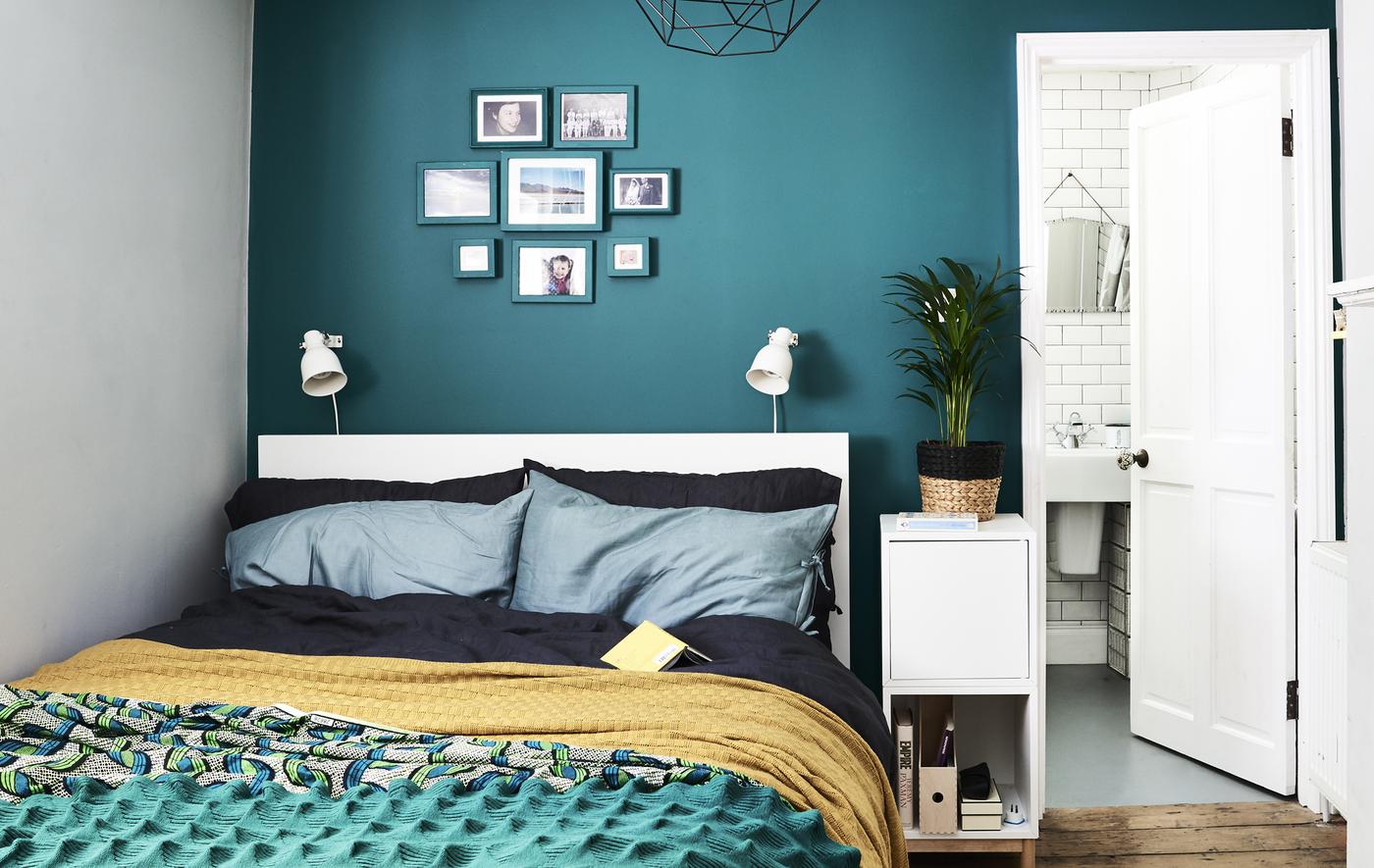 A bedroom with dark green wall and colourful bedding.