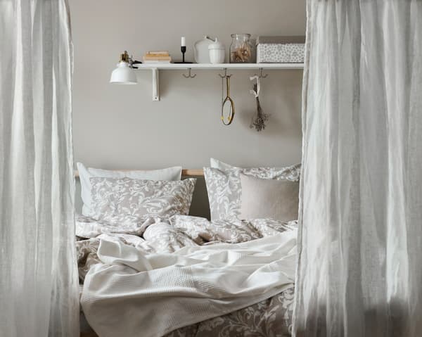 A bedroom with gray curtains, beige and white bedlinen, and matching pillows