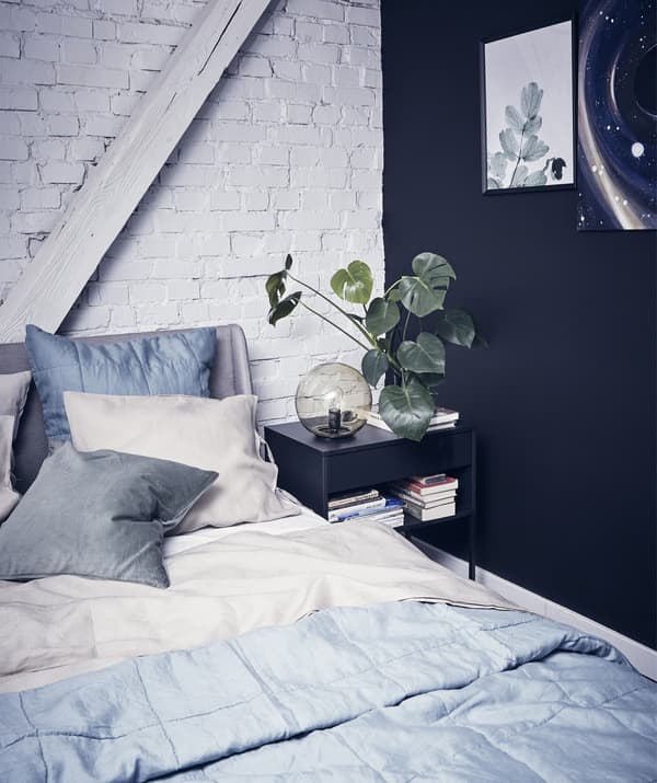 A bedroom with layered grey bedding, one black wall and one white painted brick wall.