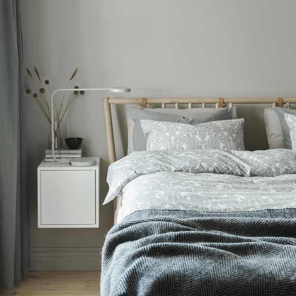 A bedroom with layers of bedding in neutral colours and a white wall-mounted bedside unit.