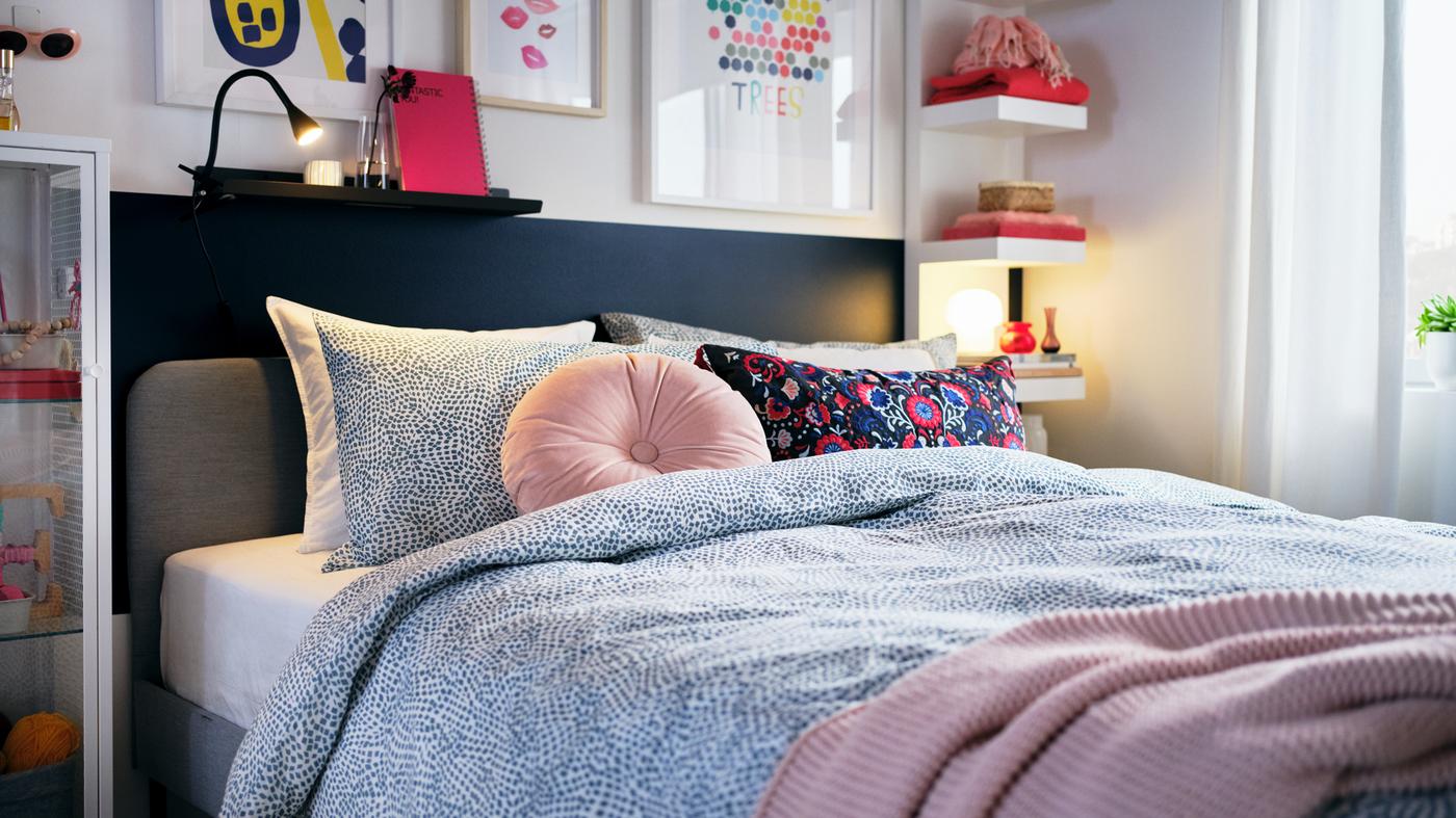 A bedroom with pops of colorful decorations, a light-grey SLATTUM bed with blue-and-white TRÄDKRASSULA bed linen.