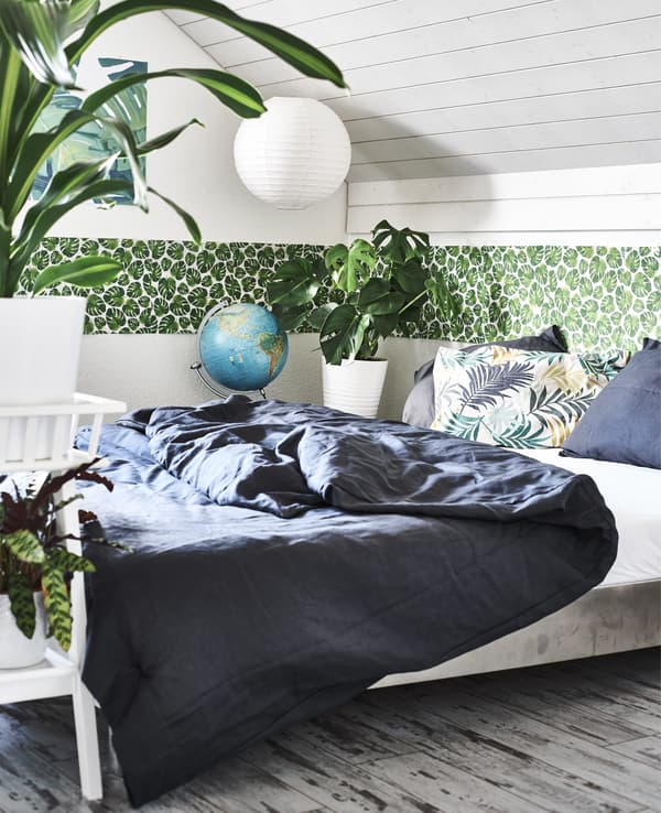 A bedroom with pot plants, green leaf border and dark bedding.
