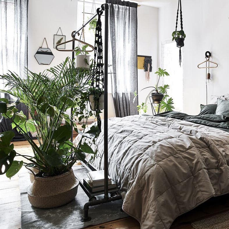 A bedroom with white walls, natural-coloured bedding and plants in wicker baskets.