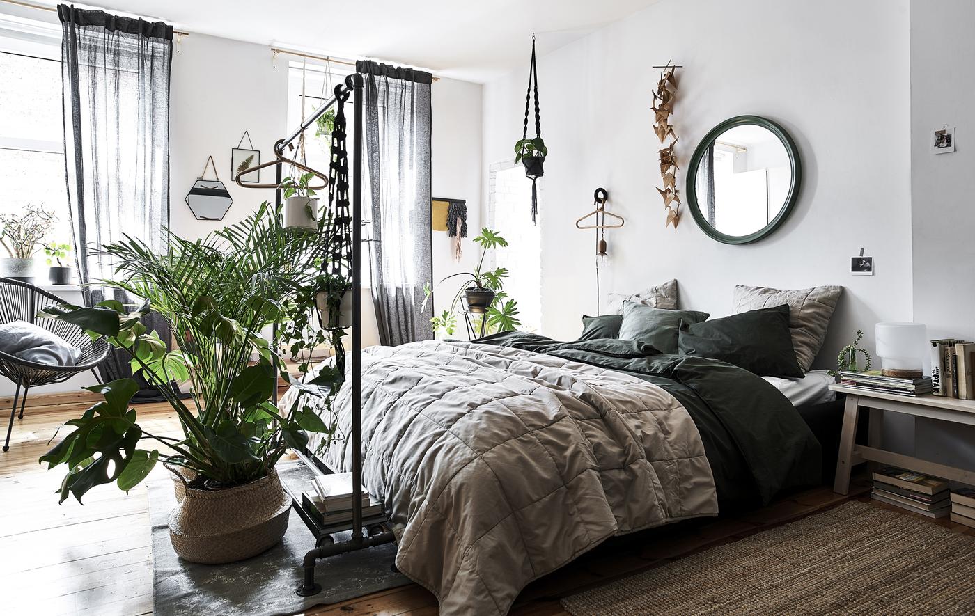 A bedroom with white walls, natural-coloured bedding and plants in wicker baskets.
