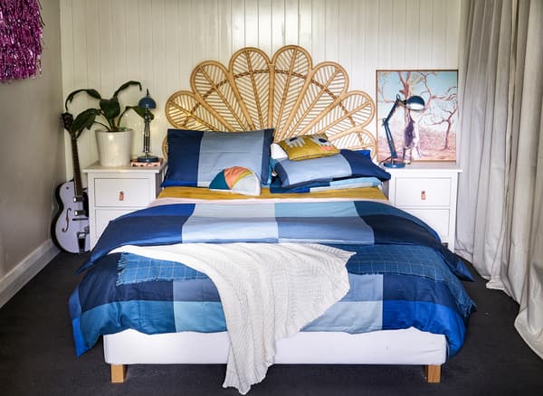 A bedroom with wicker bed head, blue bedding and white bedside tables.