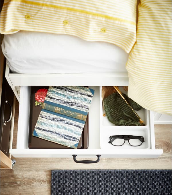 A bedside drawer pulled out with a book and glasses inside.