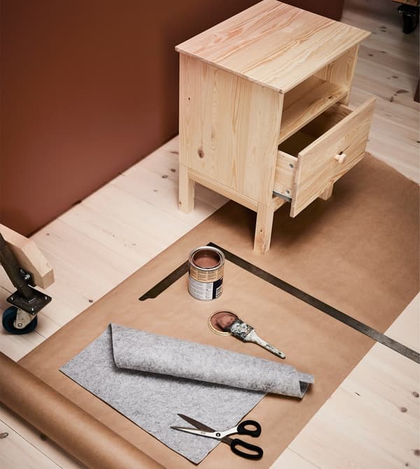 A bedside table waits to be brush painted with a tin of brown paint, and have a felt drawer liner added.